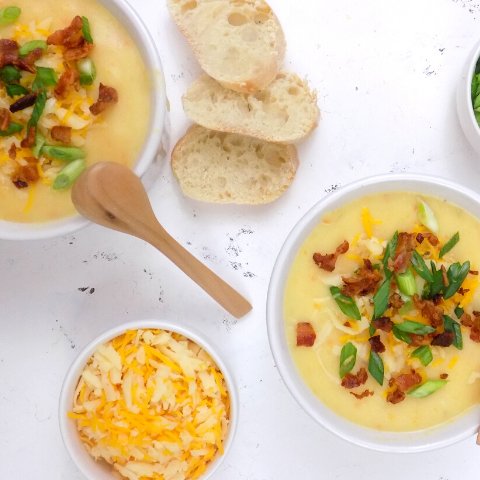 potato soup in white bowls topped with bacon, cheese and onions